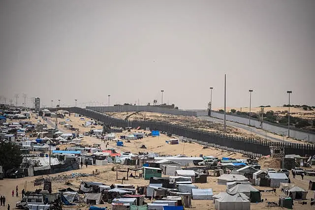 Palestinians displaced by the Israeli air and ground offensive on the Gaza Strip walk through a makeshift tent camp in Rafah, on the border with Egypt