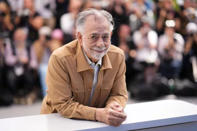 Man in a brown jacket leans on a table