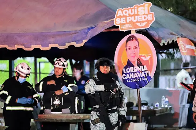 Relief workers and security forces stand next to electoral posters after the stage collapse