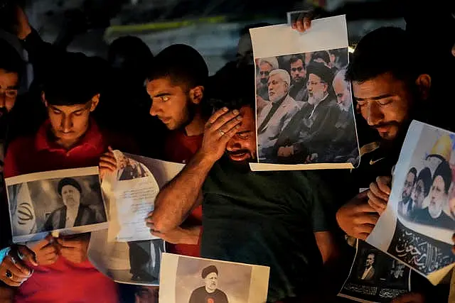 A Shiite Muslim weeps while holding photos of Iranian president Ebrahim Raisi