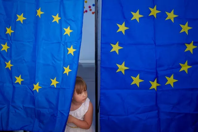 A child peers out from behind a voting curtain with the EU flag on it