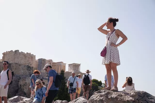 Los turistas se encuentran en una colina frente a la Acrópolis en el centro de Atenas