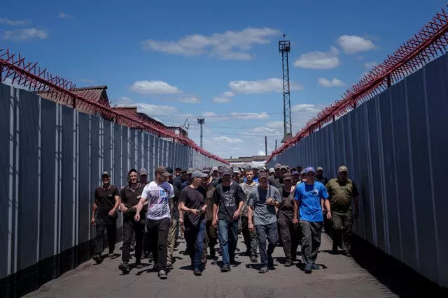 A group of men walk between high metal fences