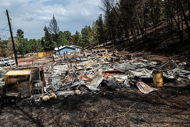 Detritos de uma casa destruída por um incêndio florestal, com árvores queimadas nas proximidades