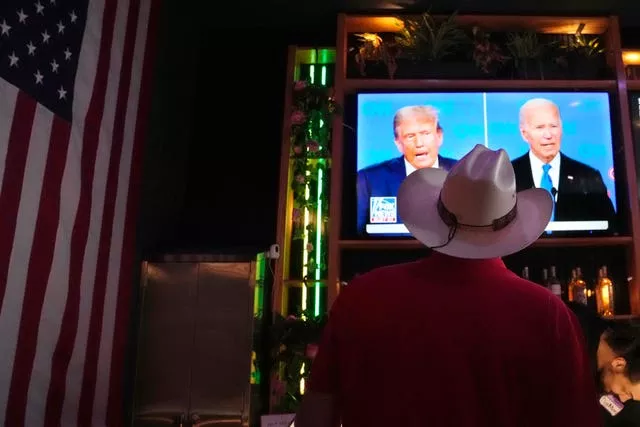 A man wearing a cowboy hat watches the presidential debate on a television screen