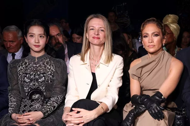 Jennifer Lopez and two other women sit with their hands on their knees