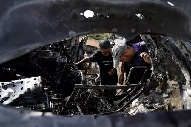 People inspect the charred remains of a car