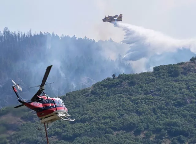 Helicopter in foreground, with a plane dropping water over forest in the background