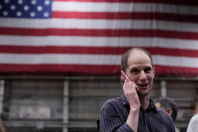 Evan Gershkovich on the phone with an American flag in the background