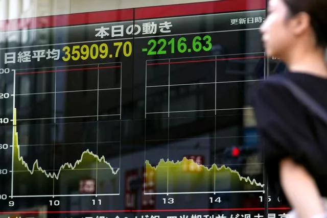 A person walks in front of an electronic stock board showing Japan’s Nikkei 225 index