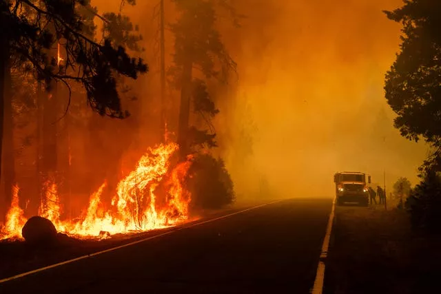 Firefighters work to keep a spot fire from growing along State Route 172 as the Park Fire burns in the Mill Creek community of Tehama County, California