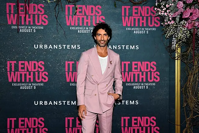 Justin Baldoni in a salmon suit in front of It Ends With Us promotional materials at the film's world premiere