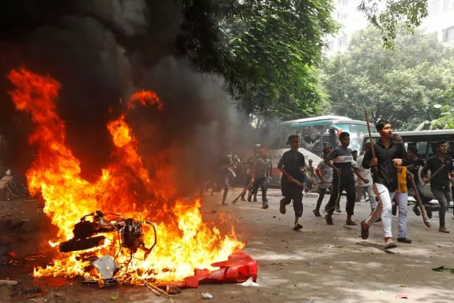 Men run past a burning vehicle inside the Bangabandhu Sheikh Mujib Medical University Hospital, set on fire by protesters during a rally against Sheikh Hasina