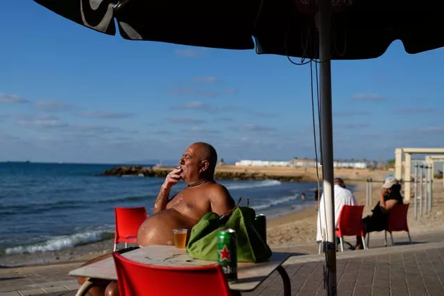 Un hombre fuma bajo una sombrilla junto al mar.