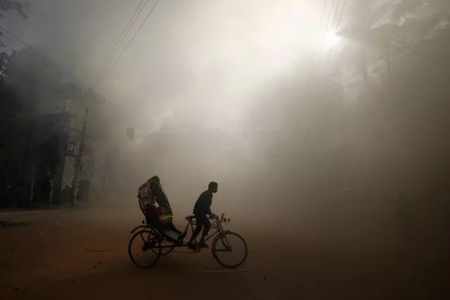 A rickshaw puller rides in the smoke caused by a burning shopping centre in Dhaka 