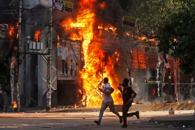 Men run past a shopping centre set on fire by protesters