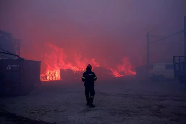 A firefighter stands in front of a burning business during a fire in northern Athens 