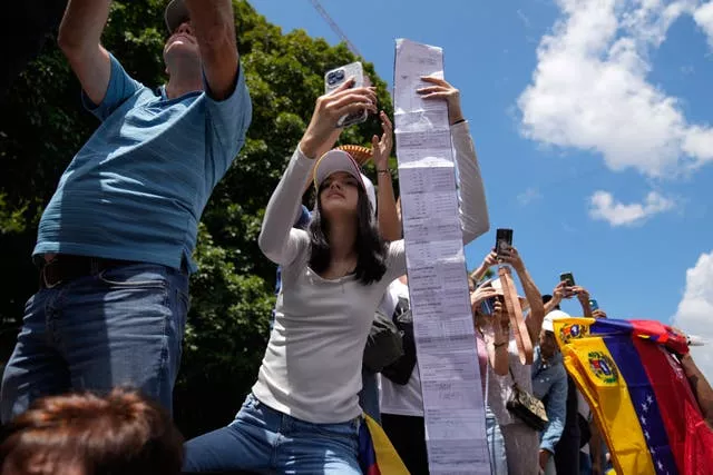 Woman in crowd holding up long sheet of paper showing a vote tally