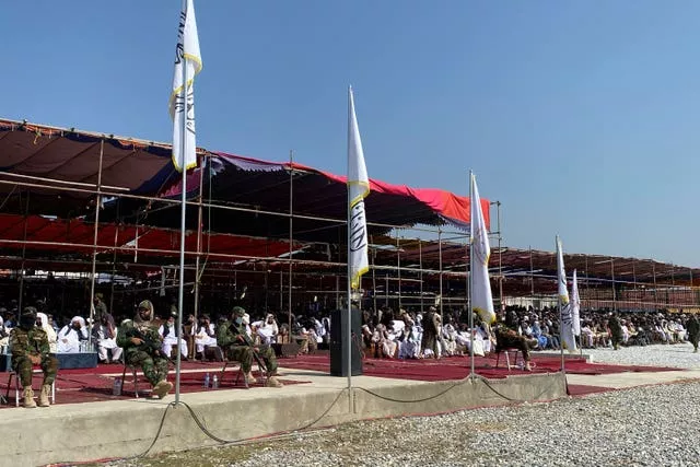 Afghan men and uniformed men sit in a covered stand