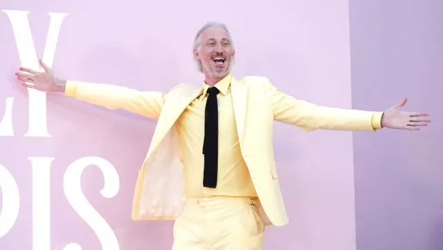 Bruno Gouery stands with his arms out in yellow suit