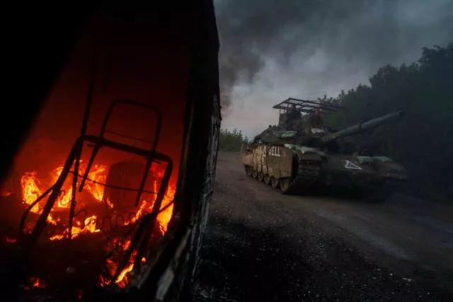 A Ukrainian tank passes by a burning car near the Russian-Ukrainian border, Sumy region, Ukraine 