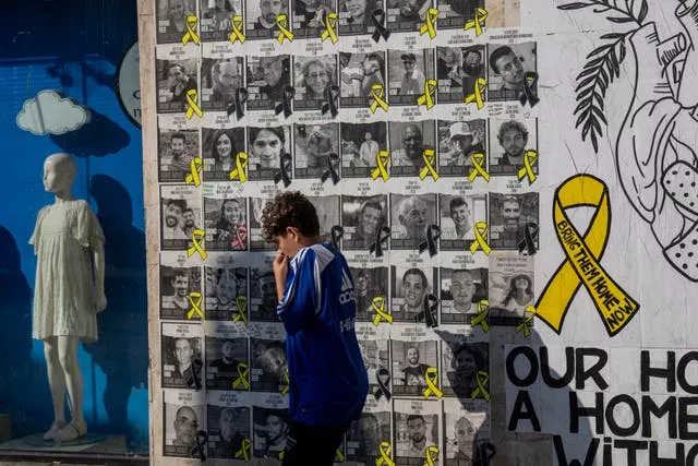 A boy walks past a wall with photos of hostages held in the Gaza Strip, in Tel Aviv