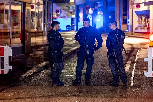 Three officers with guns stand in the street