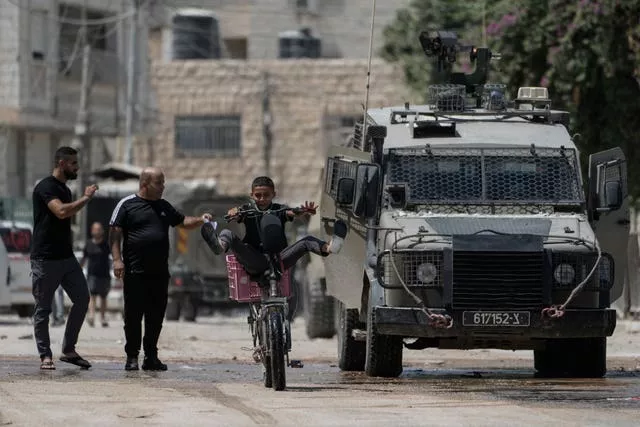 A youth rides his bicycle past an Israeli armoured vehicle