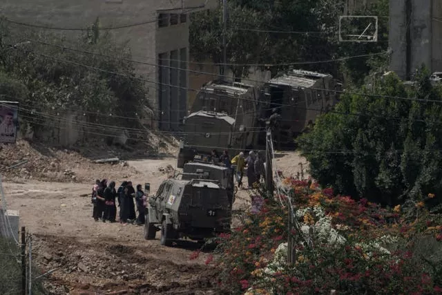 A group of people stand next to a line of military lorries