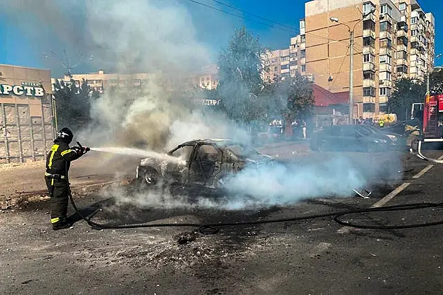 Firefighter sprays water hose at burning car on street