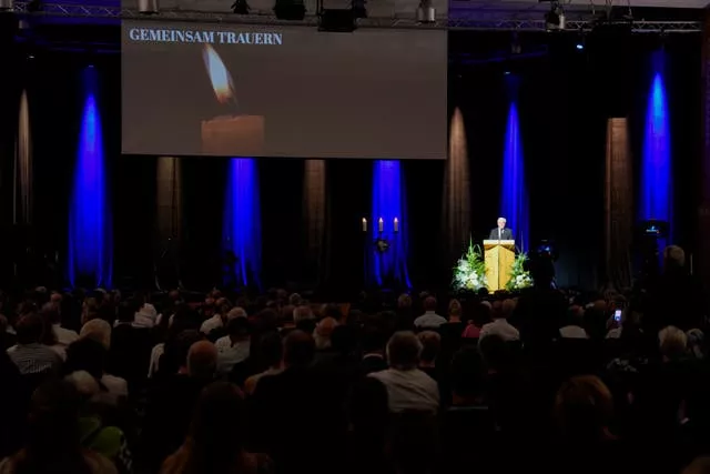 Frank-Walter Steinmeier under spotlight in the distance on a stage, with an audience in the foreground