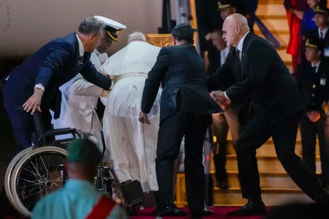 People aiding the Pope as he moves from a wheelchair