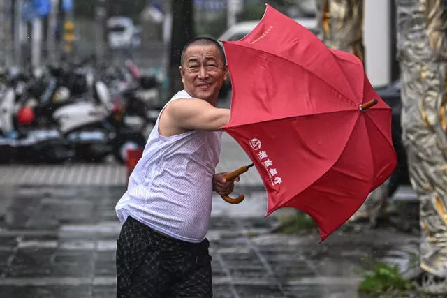 A man holding a red umbrella struggles against the wind