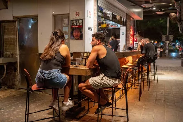 People sit in a bar near a sign calling for the release of hostages held by Hamas