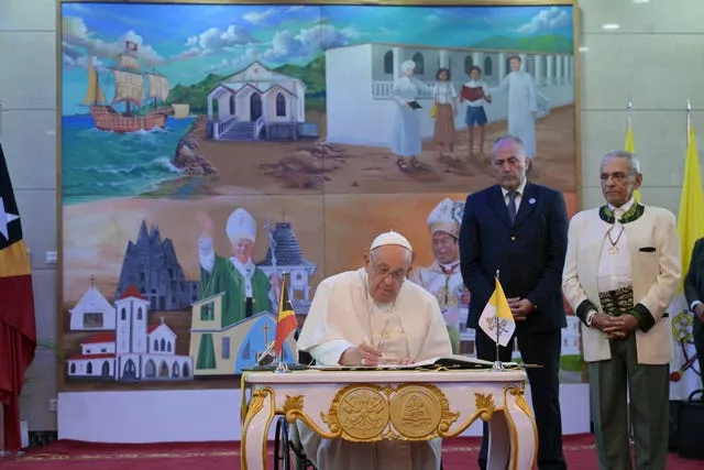 Pope Francis signs a guestbook as East Timor’s President Jose Ramos-Horta, right, looks on at the Presidential Palace in Dili, East Timor