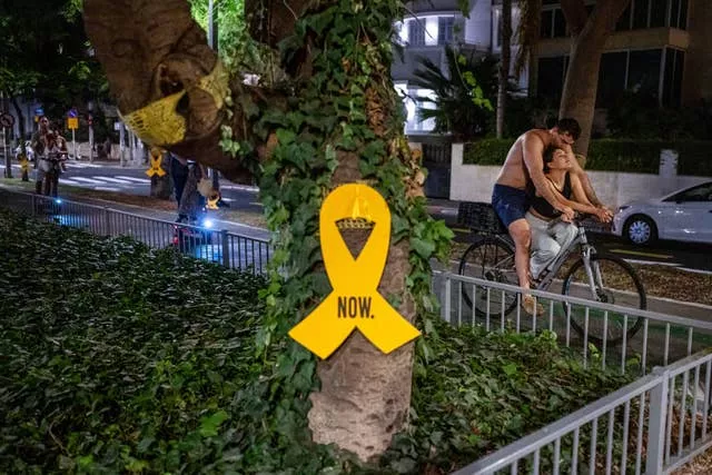 A couple rides a bicycle near a yellow ribbon sign calling for the release of hostages