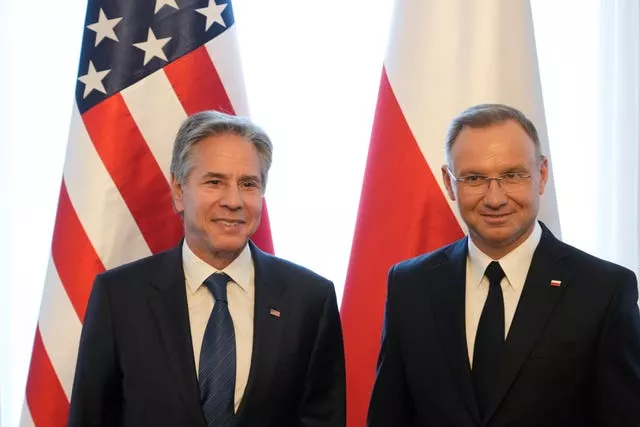 Antony Blinken and Andrzej Duda smile as they stand next to each other in front of their flags