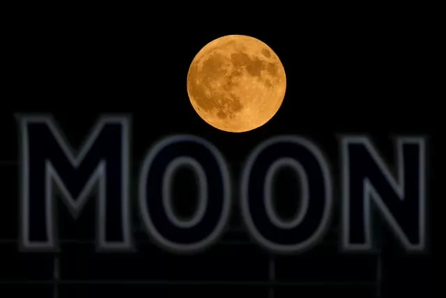 The full moon rises in the over a beer sign in the outfield at Kauffman Stadium 