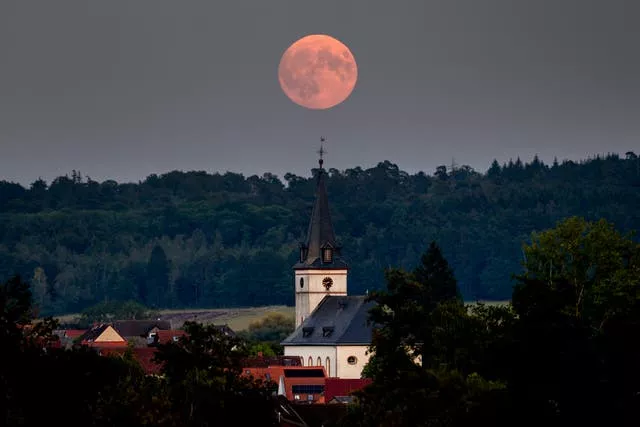 The full Harvest moon rises behind the church in Wehrheim near Frankfurt