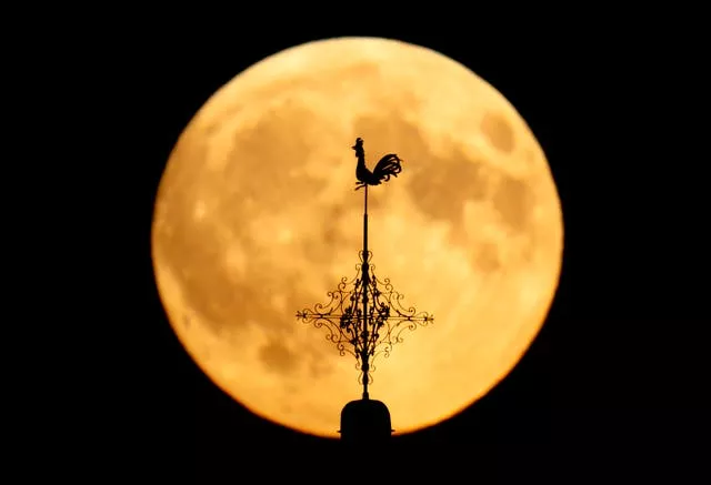 A weathervane on a church is silhouetted in front of the rising moon in Wehrheim near Frankfurt