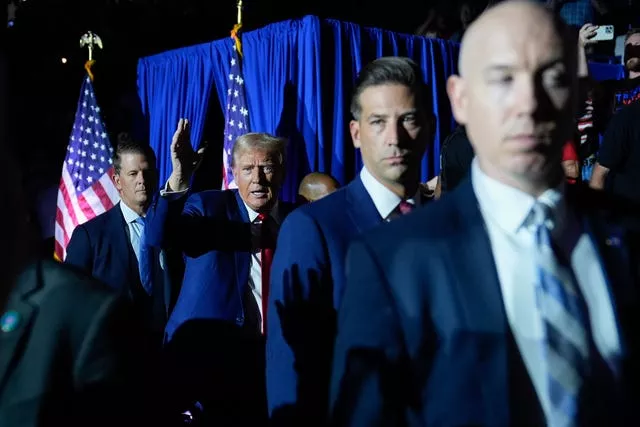 Donald Trump waves as he enters an event surrounded by Secret Service agents