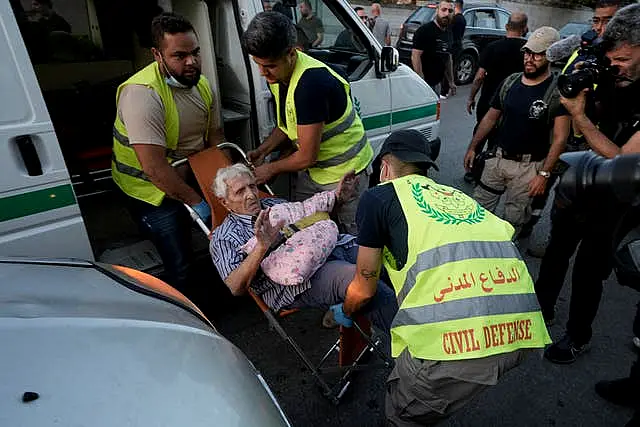 Civil defence workers carry an elderly man fleeing the south as he arrives at a school turned into a shelter in Beirut 