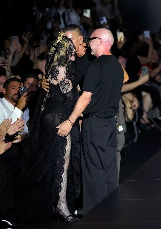 Madonna wearing black, and two men wearing black, hug each other