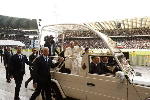 Pope Francis waving from his popemobile, which is surrounded by security personnel