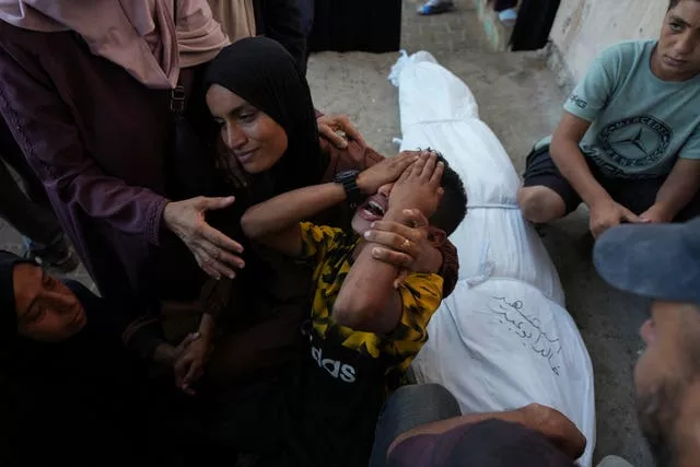 A boy covers his face and screams in grief in a woman's arms