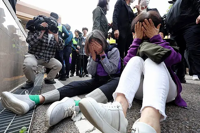 Bereaved family members of the victims of the crush sit with their hands held to their faces outside court 