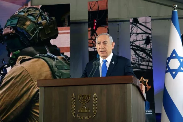 Benjamin Netanyahu speaking at lecturn, beside Israeli flag