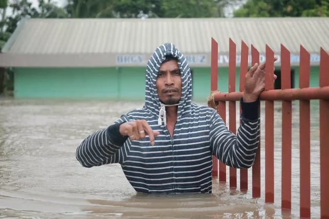 Someone waist-deep in water holds onto a fence