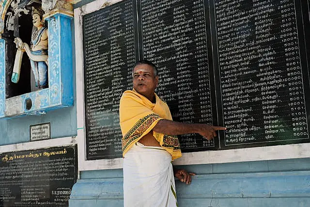 A priest points out Kamala Harris's name on a plaque