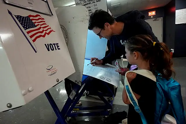 Benay Gould, seven, watches as her father Charles Herschel marks his ballot at PS M811, The Mickey Mantle School in New York 